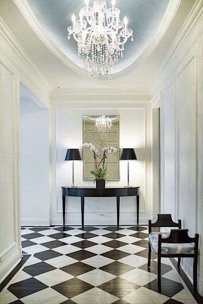 A hallway with a checkered floor and a chandelier.