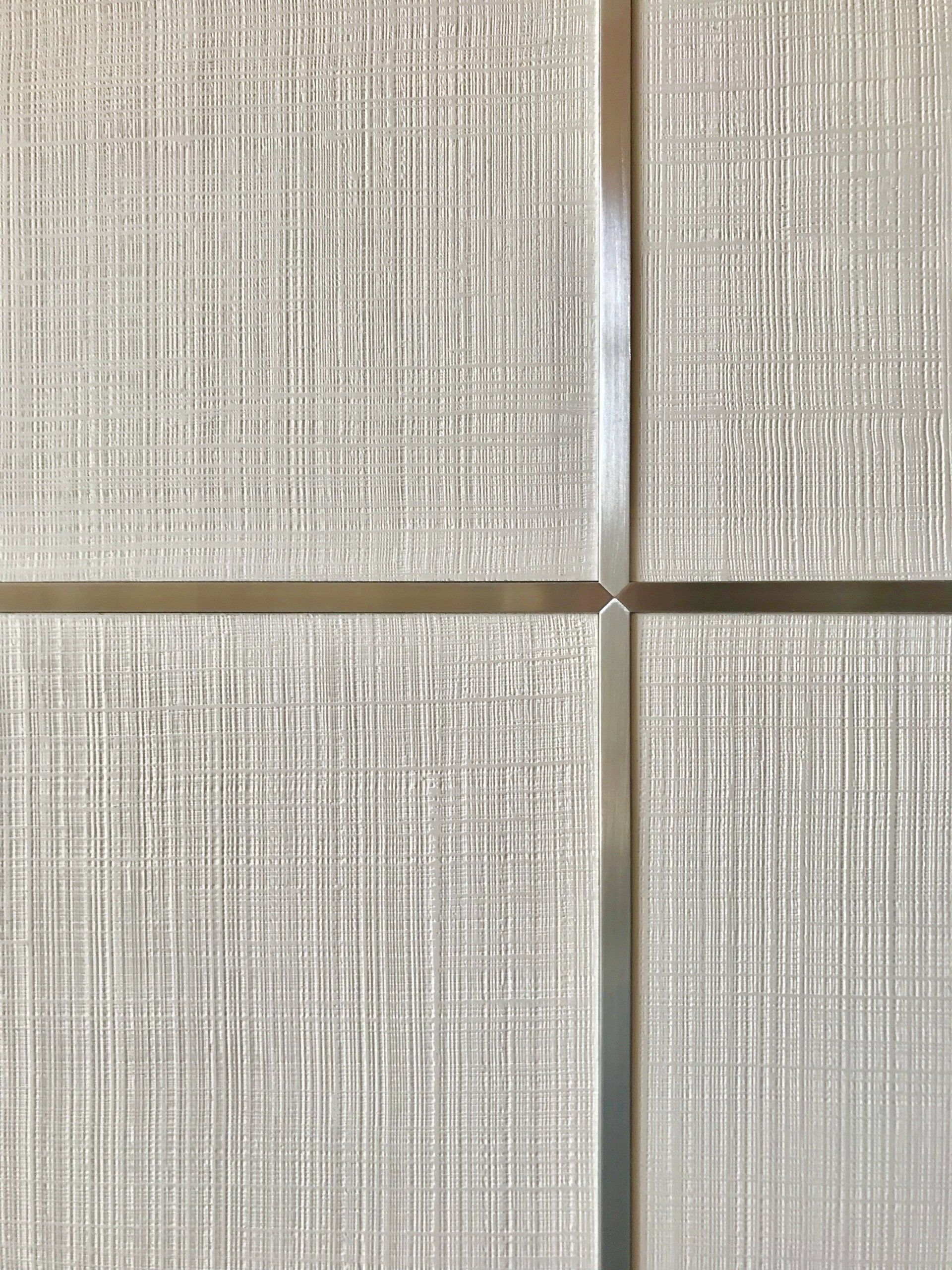 A close up of a white tile wall with a stainless steel trim.