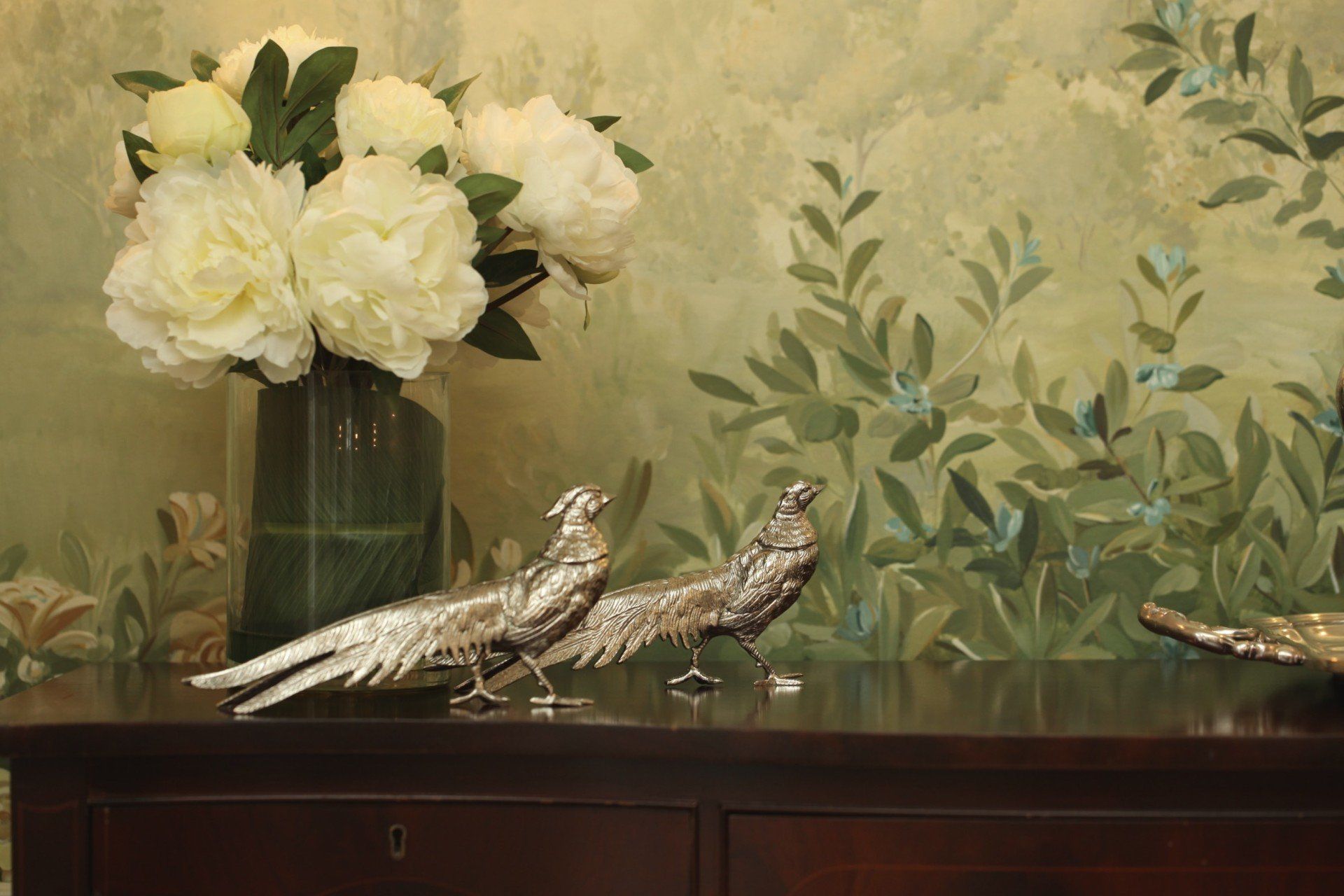 A vase of white flowers is sitting on a table next to two silver birds.