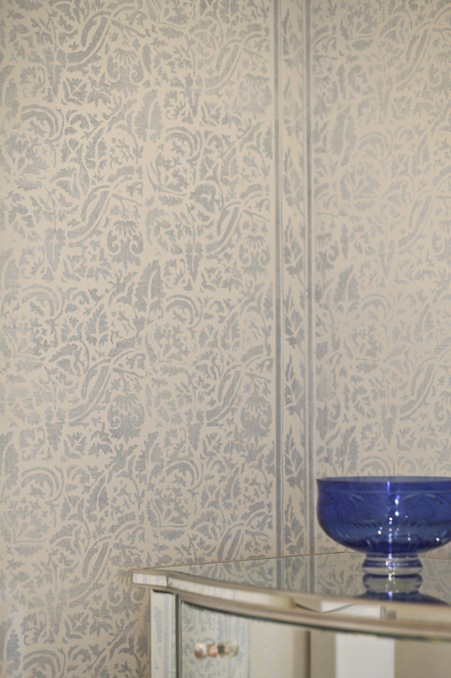 A blue bowl is sitting on a table in front of a wall with a pattern on it.