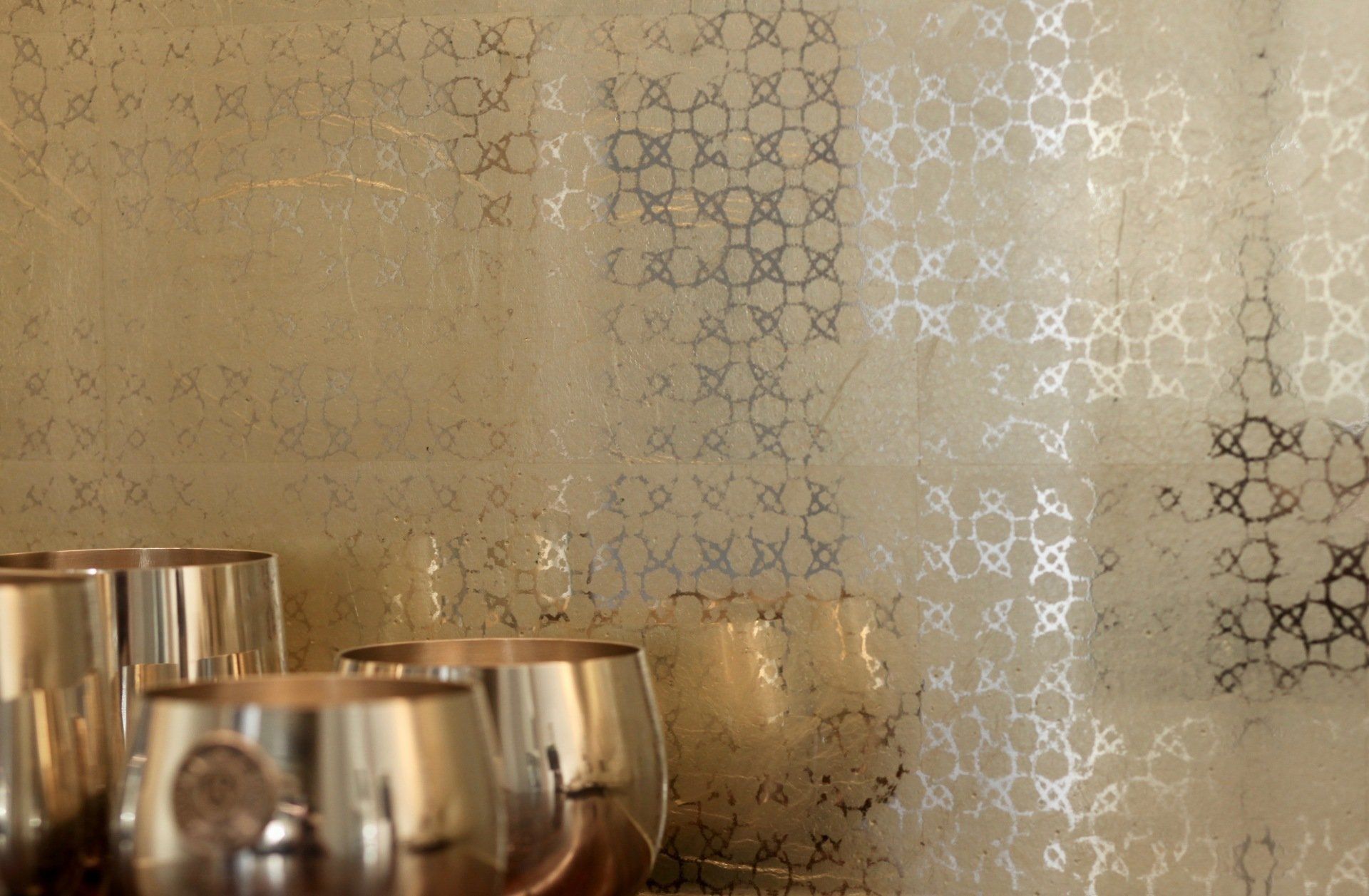 A row of wine glasses are sitting on a table in front of a wall with a pattern on it