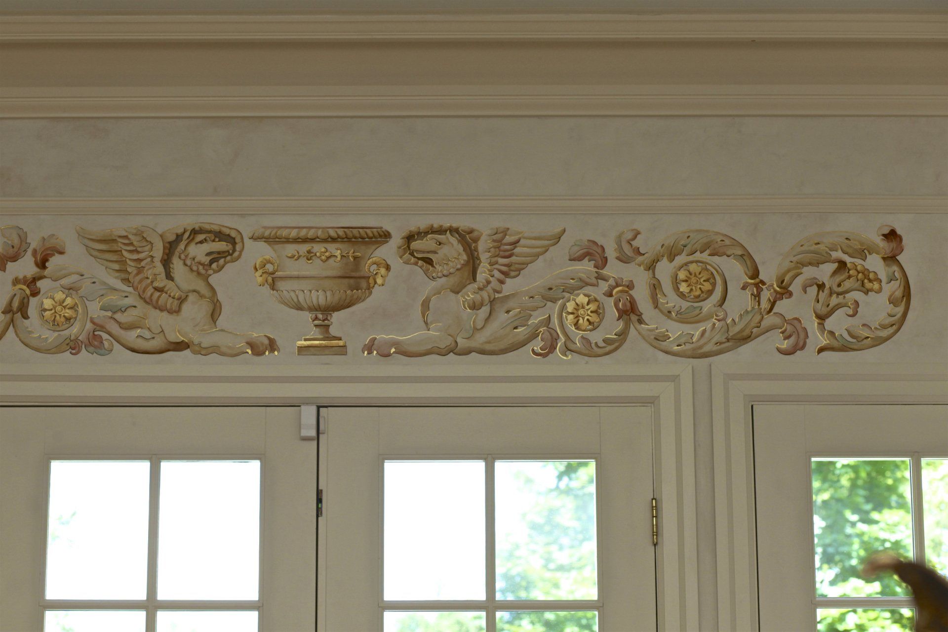 A cat is standing in front of a window with a painting on the wall above it.