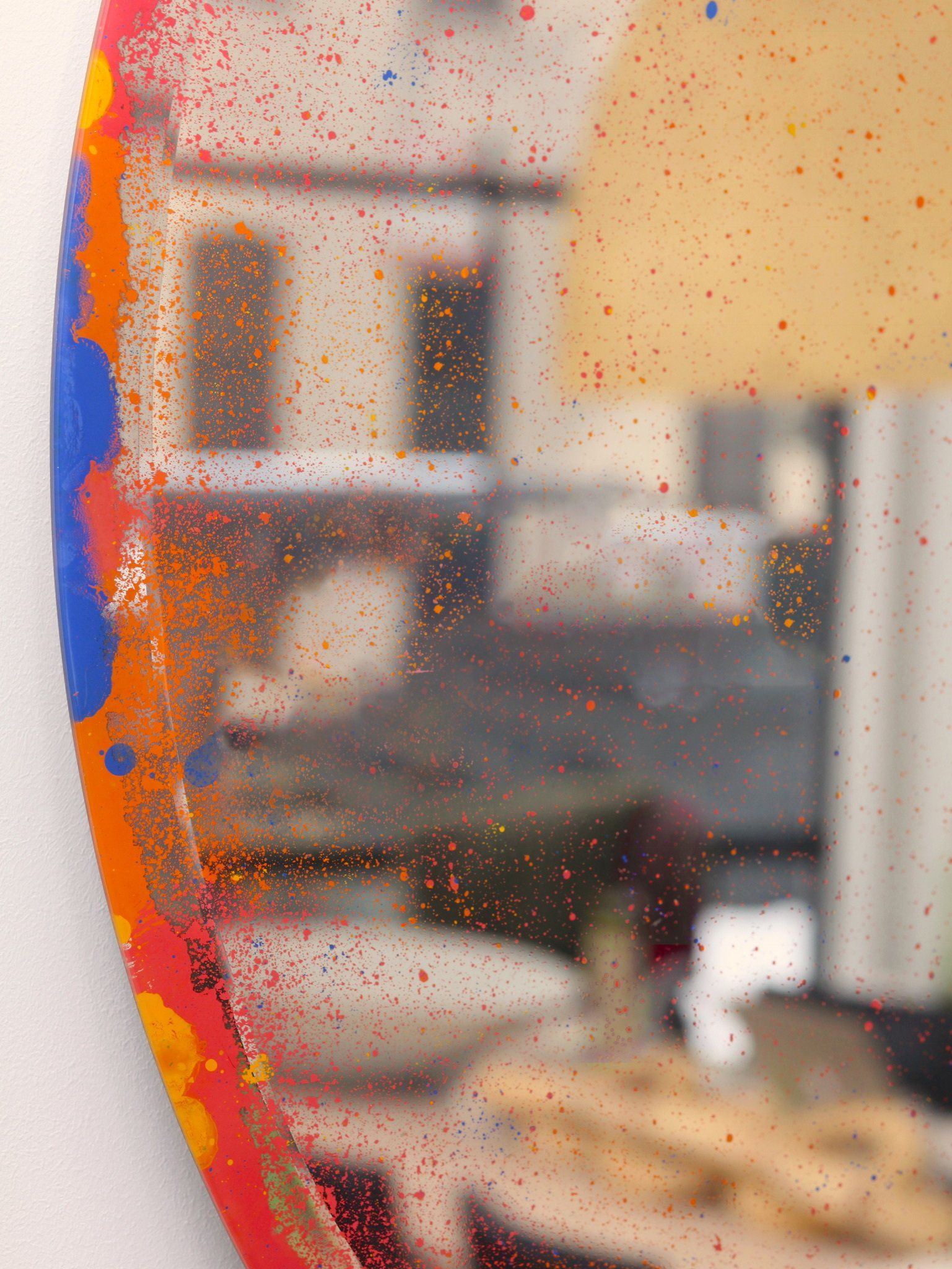 A round mirror with a colorful frame is hanging on a wall.