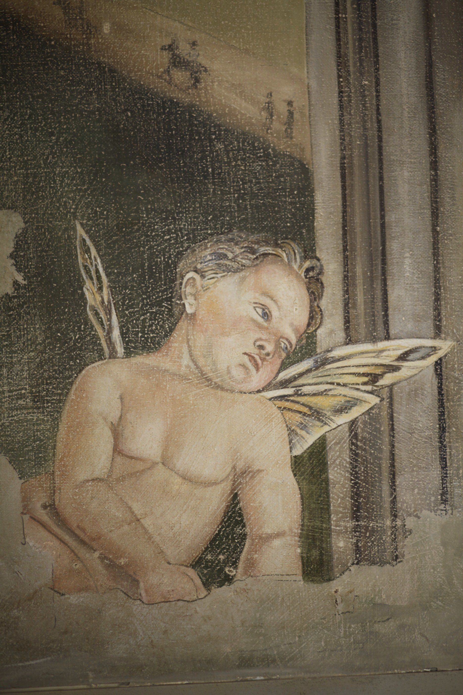 A close up of a painting of a cherub with wings on a wall.