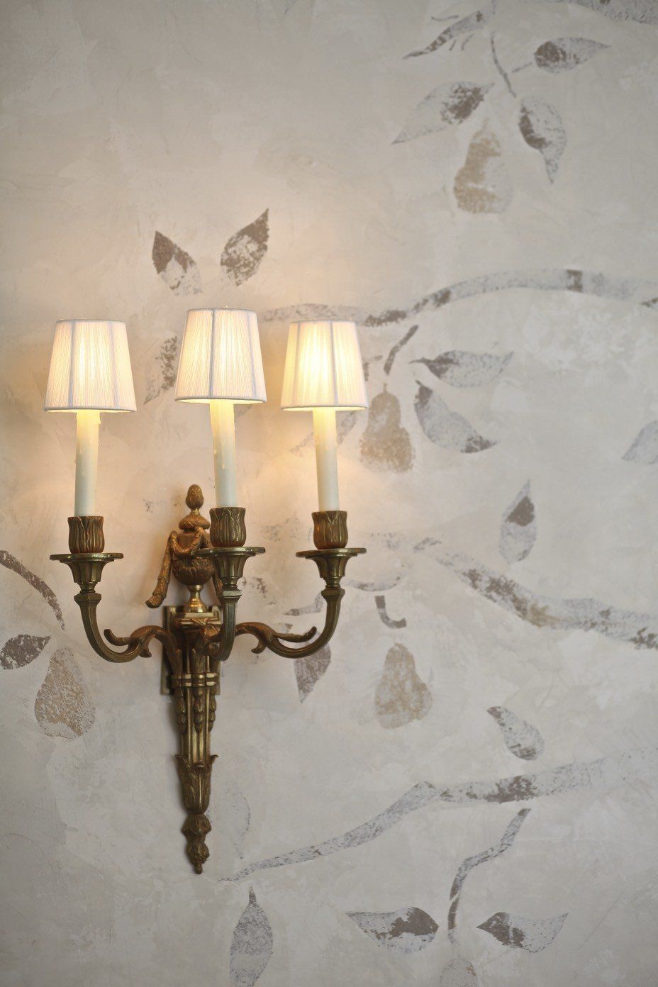 A wall light with three candles on it is hanging on a wall.