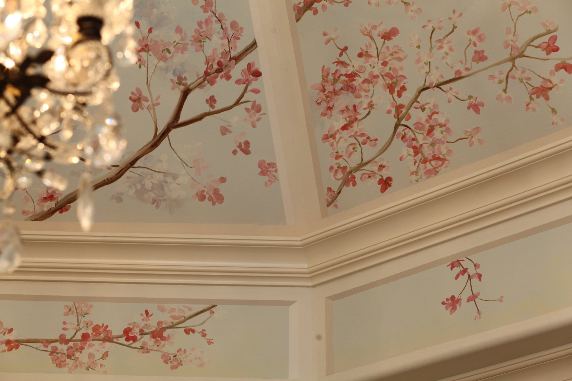 A chandelier is hanging from the ceiling of a room with cherry blossoms painted on it.
