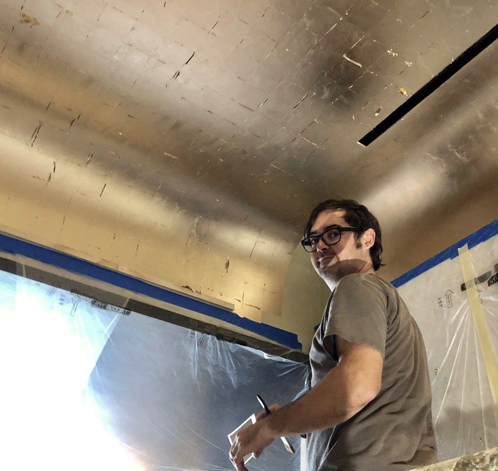A man wearing glasses is standing in front of a gold ceiling