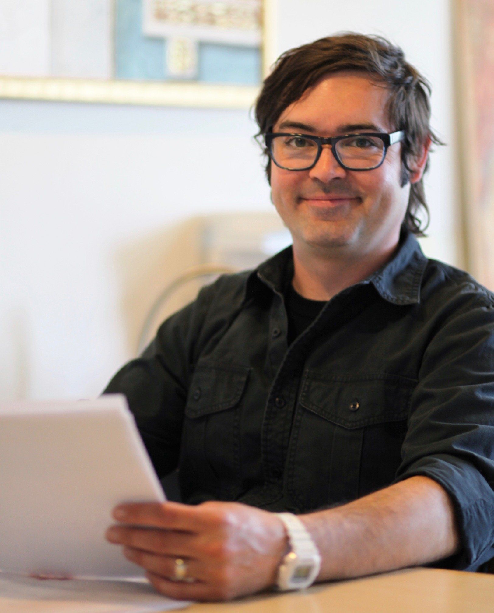 A man wearing glasses is sitting at a table holding a piece of paper