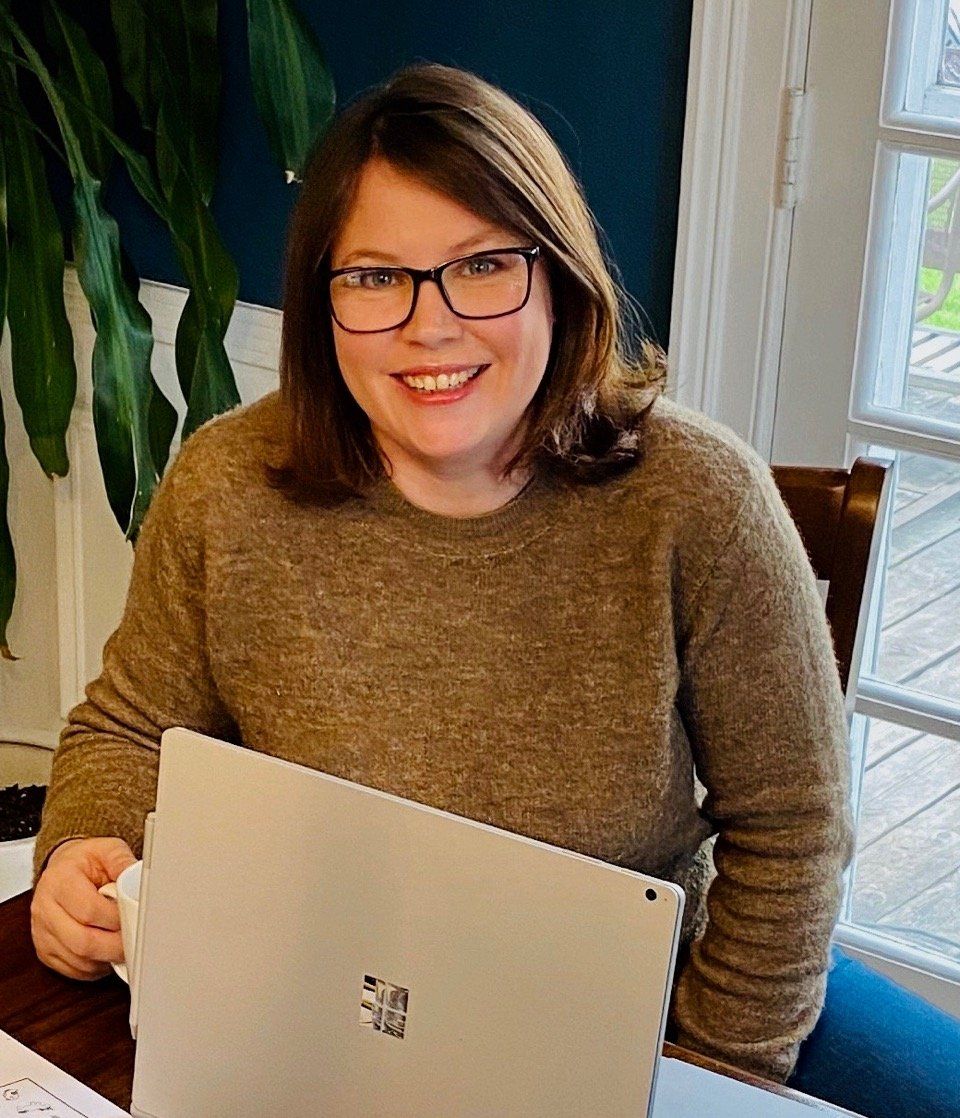 A woman wearing glasses is sitting at a table with a laptop.