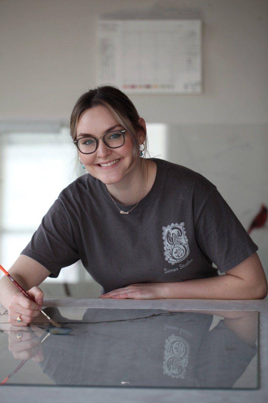A woman is sitting at a table holding a brush and smiling.