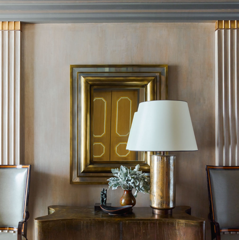 A lamp sits on a table in front of a picture of a door