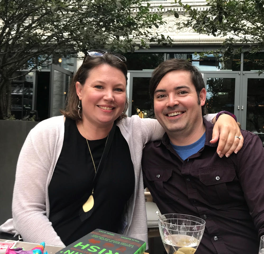 A man and a woman are posing for a picture while sitting at a table