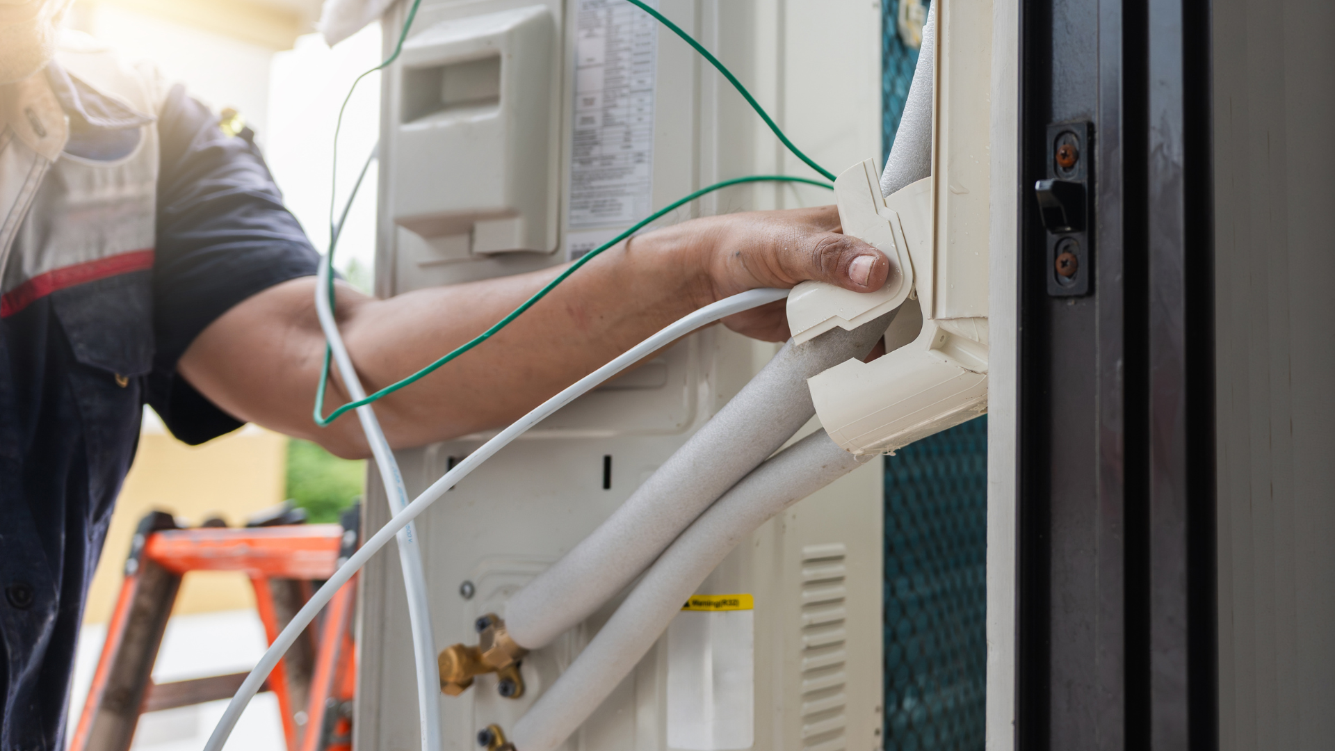 HVAC technician installing air conditioner components outdoors. Hand connecting white and green wires.