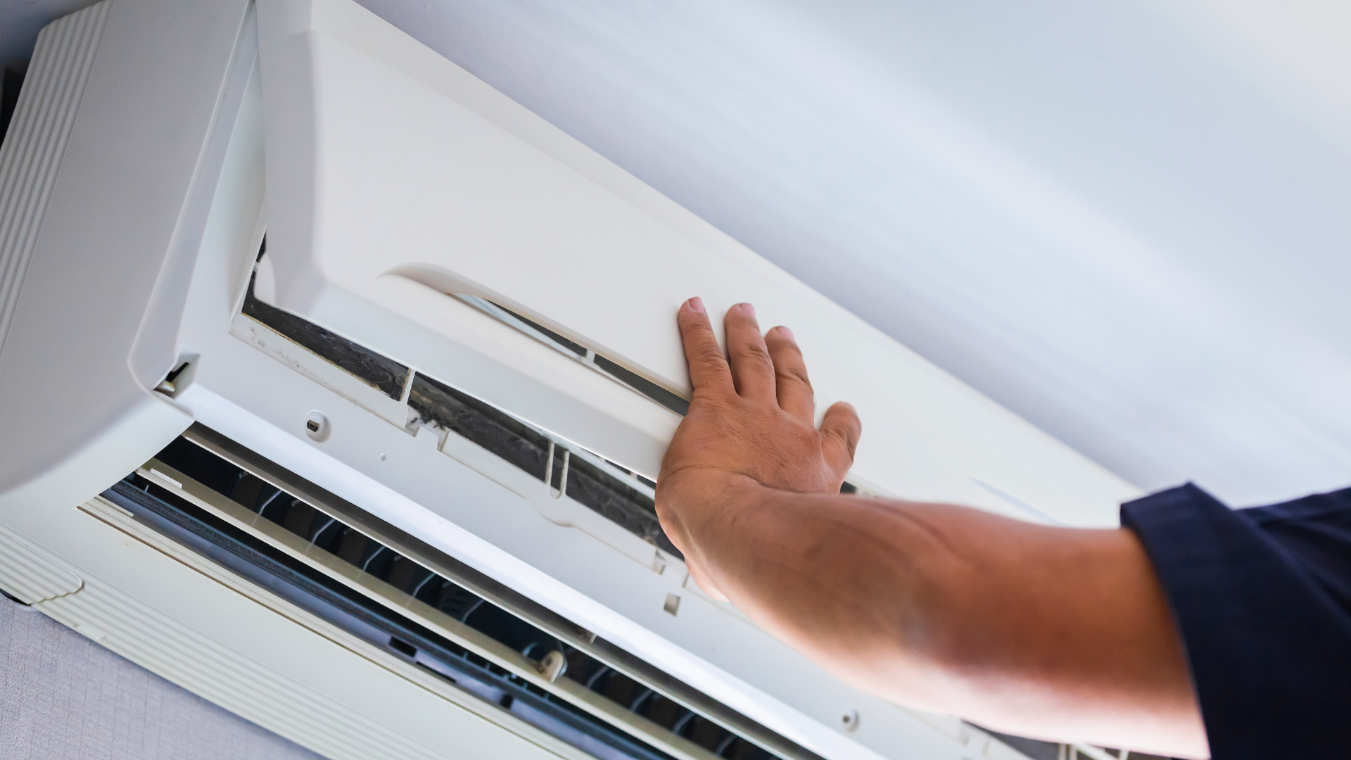 Hand inspecting a white wall-mounted air conditioning unit.