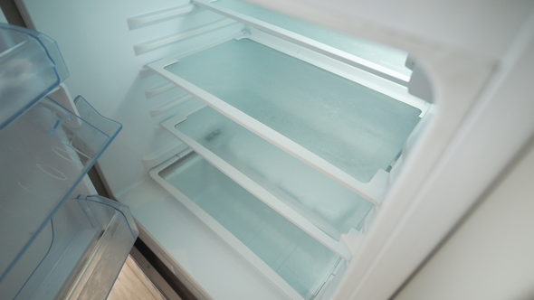 Empty refrigerator interior, showing shelves and cold, light-blue lighting.