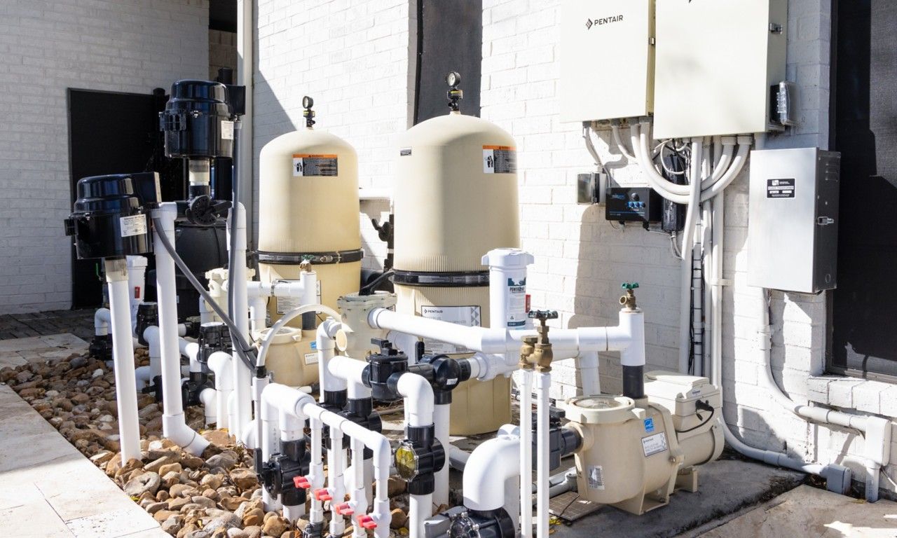 Pool filter system with beige tanks, black pumps, white pipes, and electrical boxes.