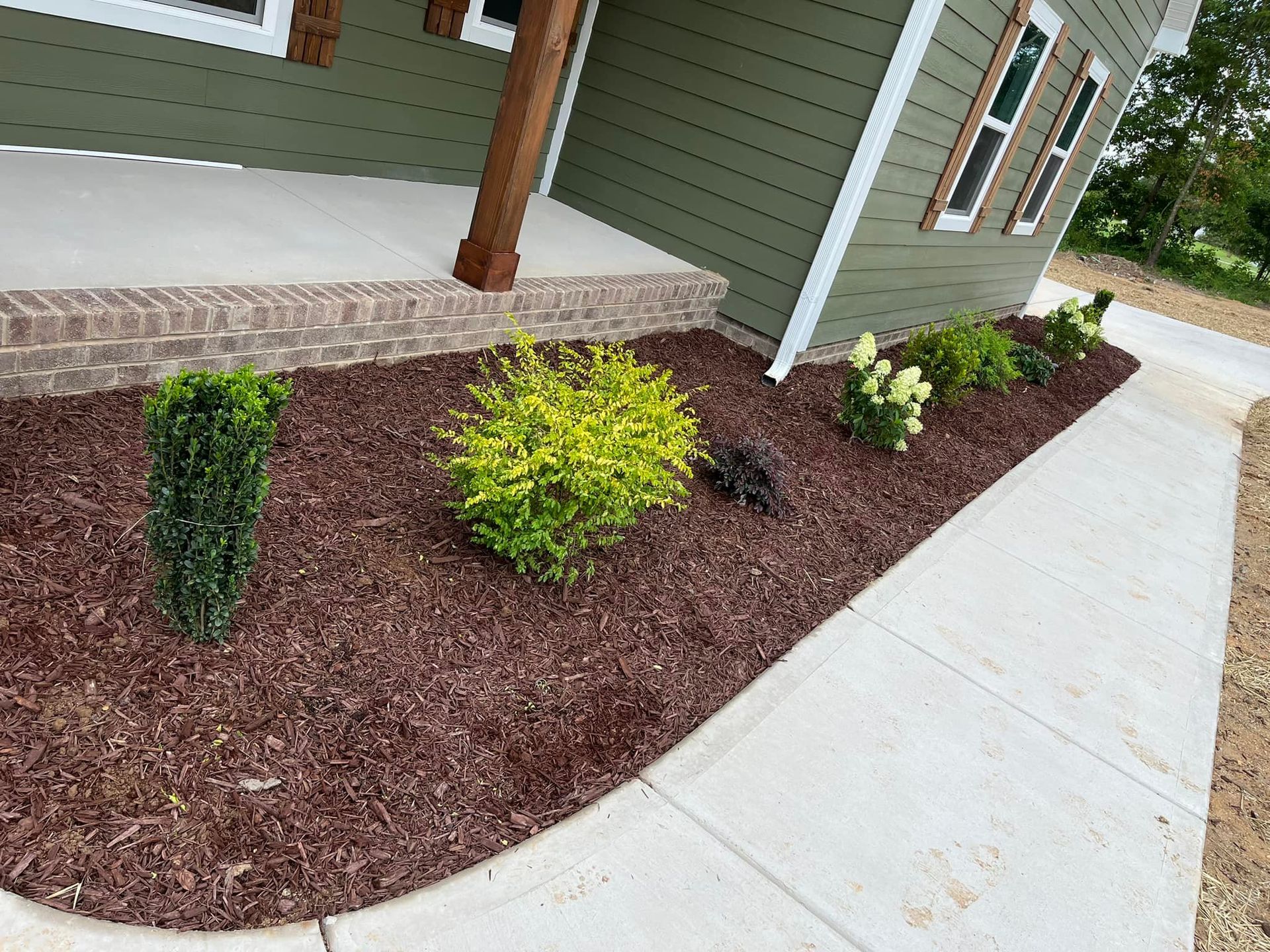Green house with a flower bed of shrubs and mulch next to a sidewalk.