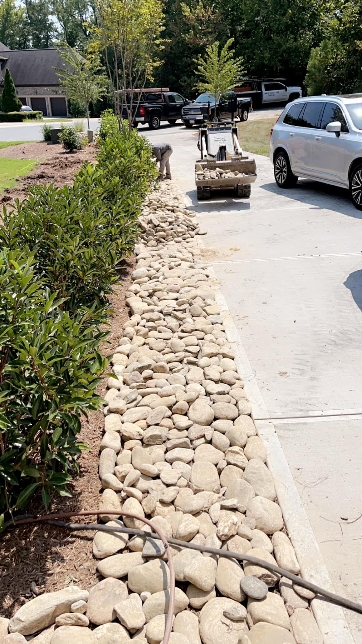 A rock border along a driveway with green bushes and a small construction vehicle.