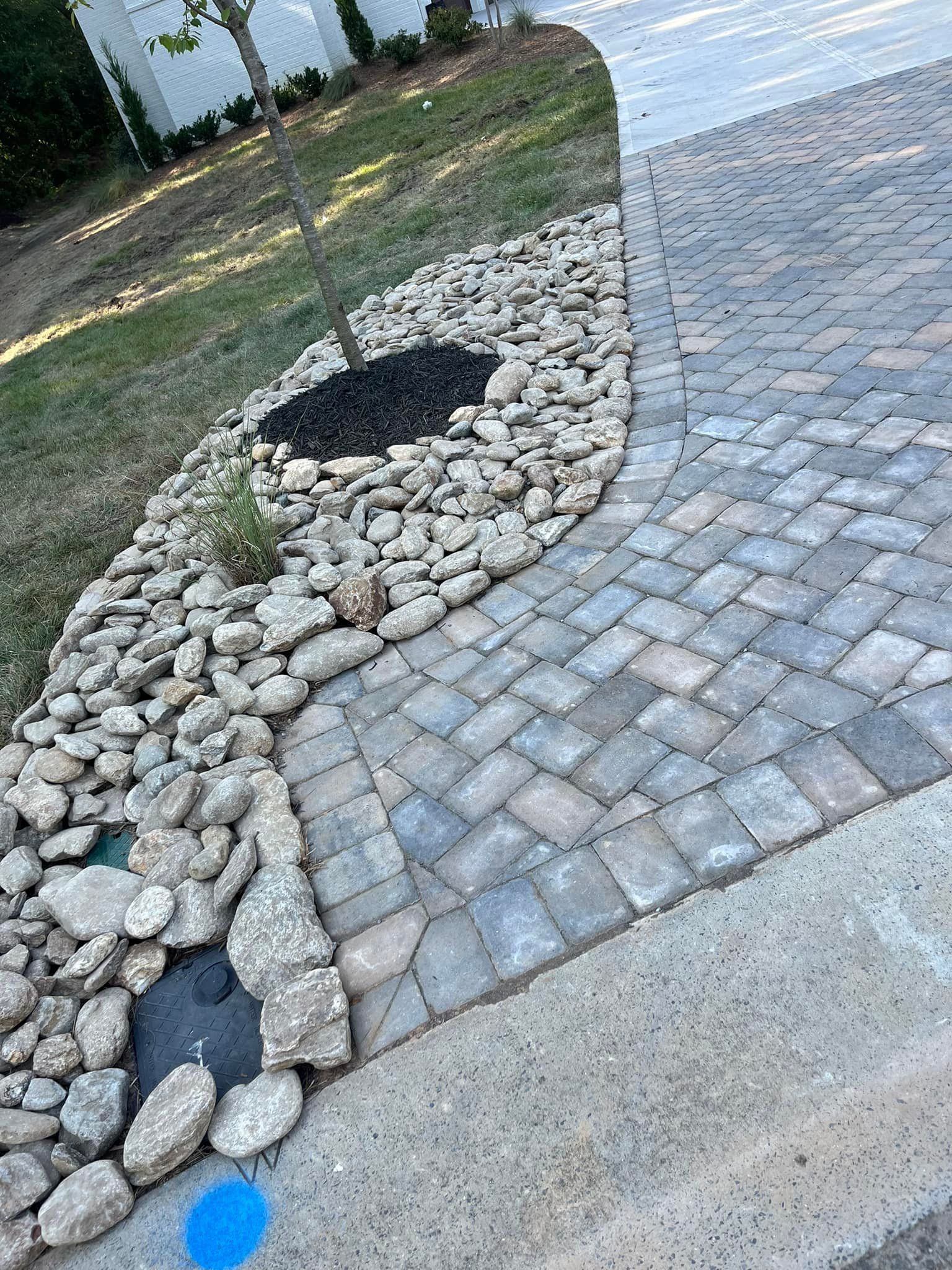 Stone pavers border a rock garden and driveway with a tree.