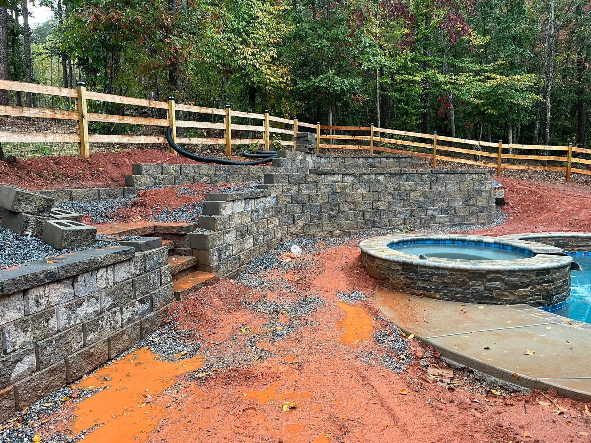 Stone retaining walls, stairs, and a hot tub surround a pool under construction