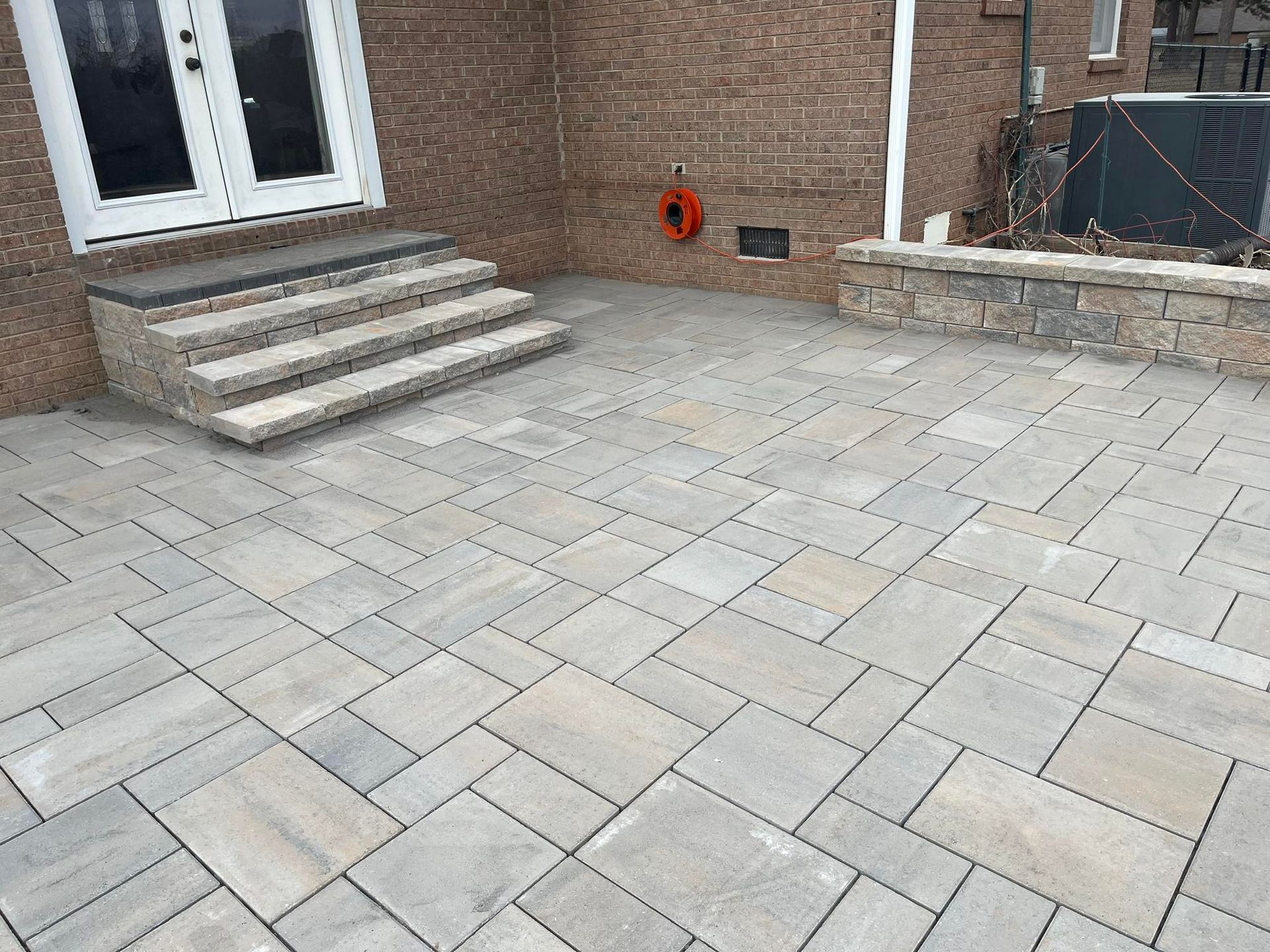 A paved patio with steps leading to double doors of a brick house.