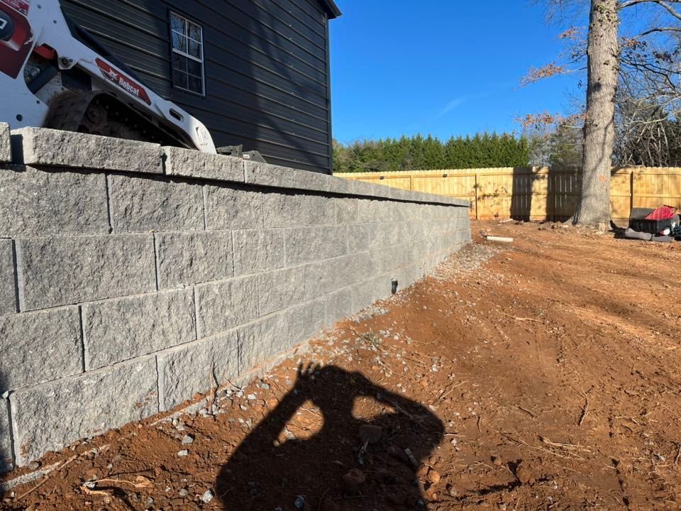 Gray retaining wall next to a dark house; a shadow of a person is in the foreground.