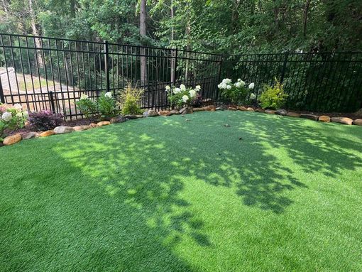 A green, artificial lawn in a backyard, framed by a black fence and flowerbeds.