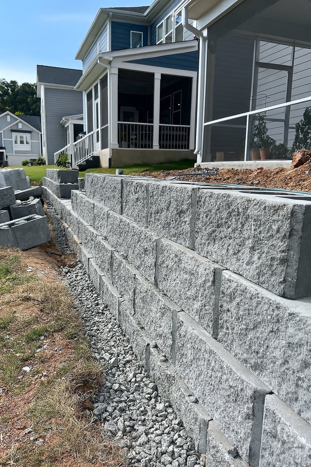 Gray retaining wall under construction in front of a two-story house.