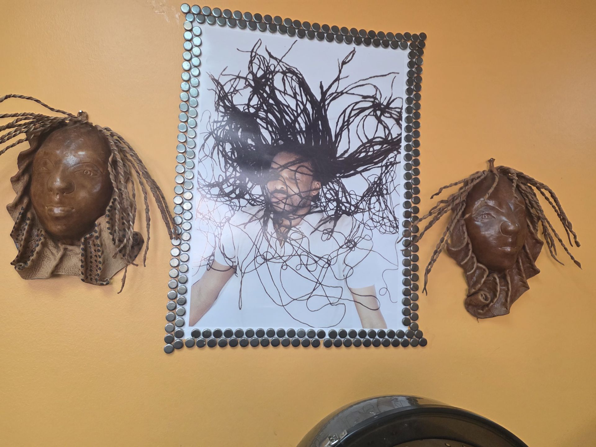 Yellow wall with a photo of a person with flying hair surrounded by metal objects, flanked by two mask-like faces.