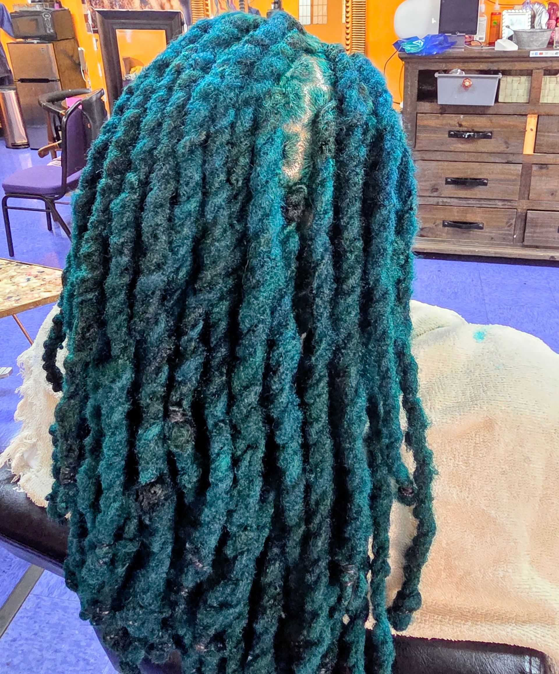 Person with vibrant teal-colored dreadlocks in a salon setting.