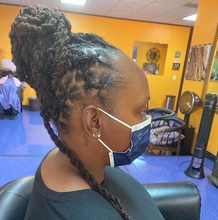 Woman with locs pulled up in a bun, wearing a mask, seated in a salon.
