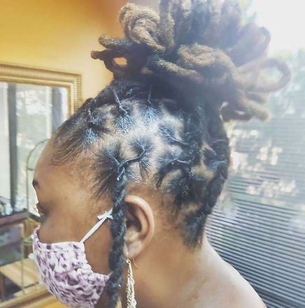 Person with dark skin and locs, wearing a face mask and a bun, with locs down the side.