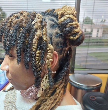 Woman with brown and black locs, some styled into buns, in a salon setting.