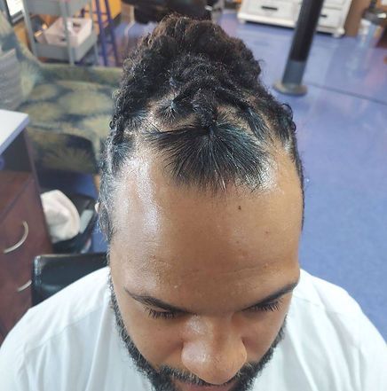 Man with braided hair in a bun, close-up. He wears a white shirt, in a barbershop.