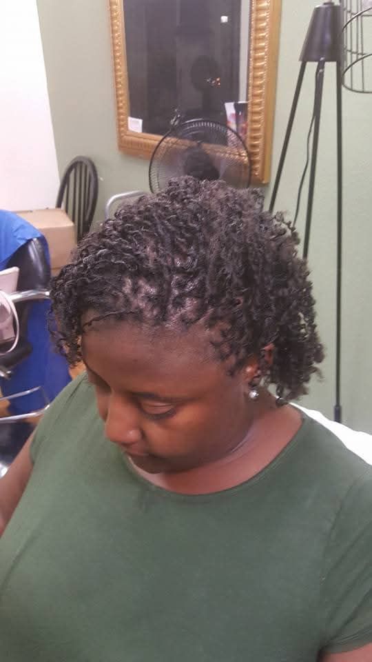 Woman with small, dark twists hairstyle; green shirt; in salon setting.