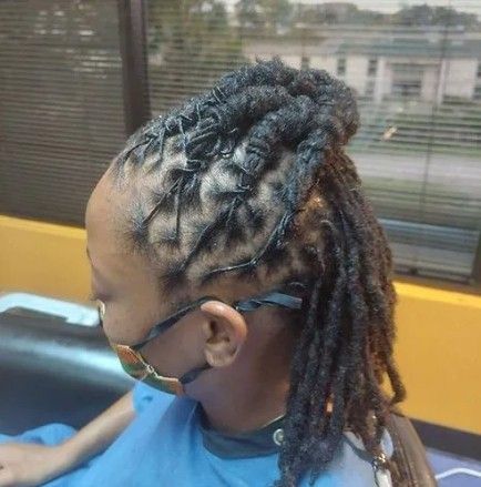 Man with braided hair in a bun, close-up. He wears a white shirt, in a barbershop.