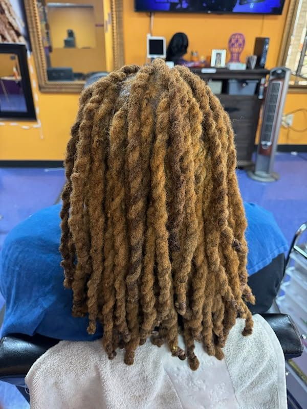 Person with long, blonde and brown locs in a salon chair, facing away from the camera.