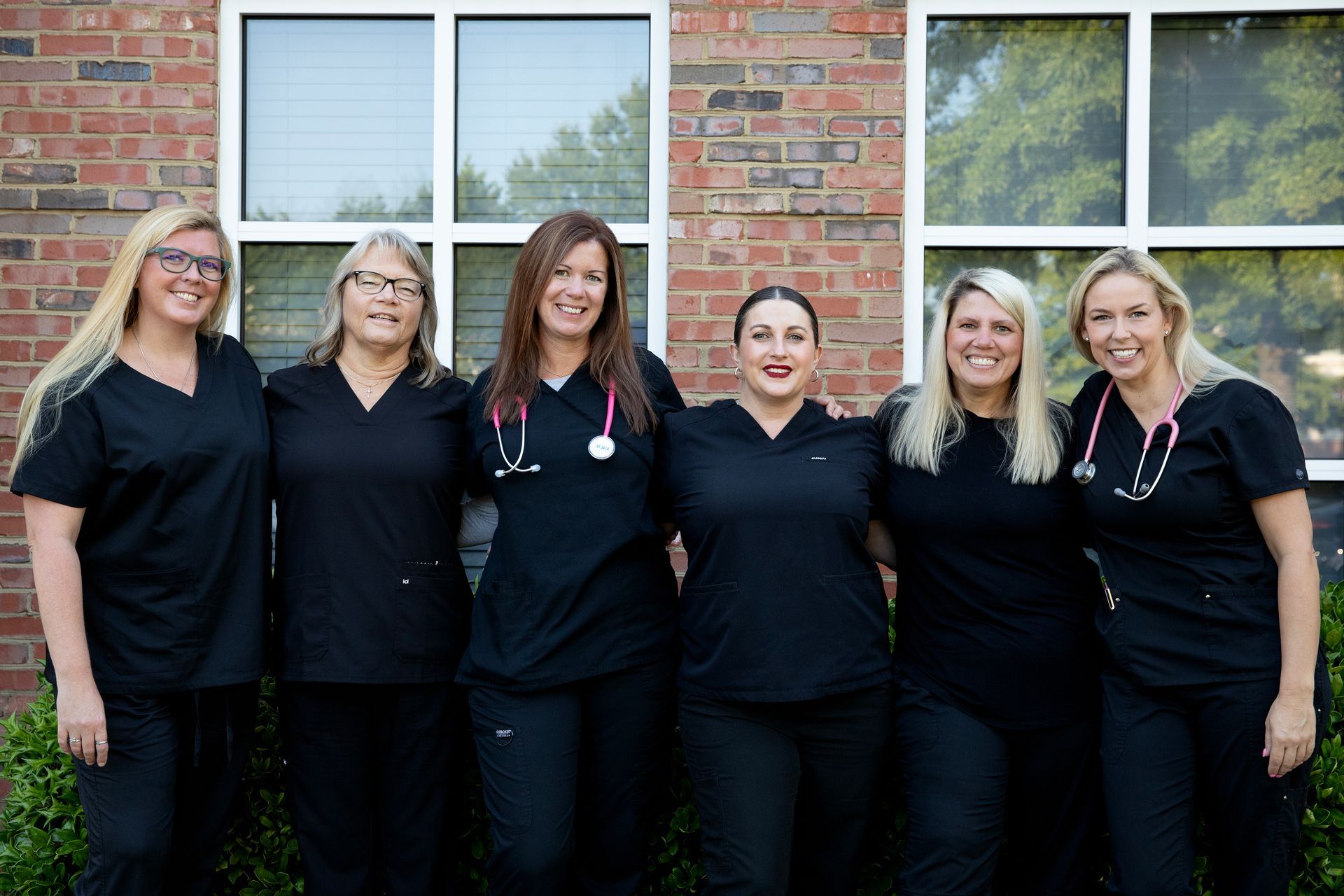 A group of nurses are posing for a picture in front of a brick building.