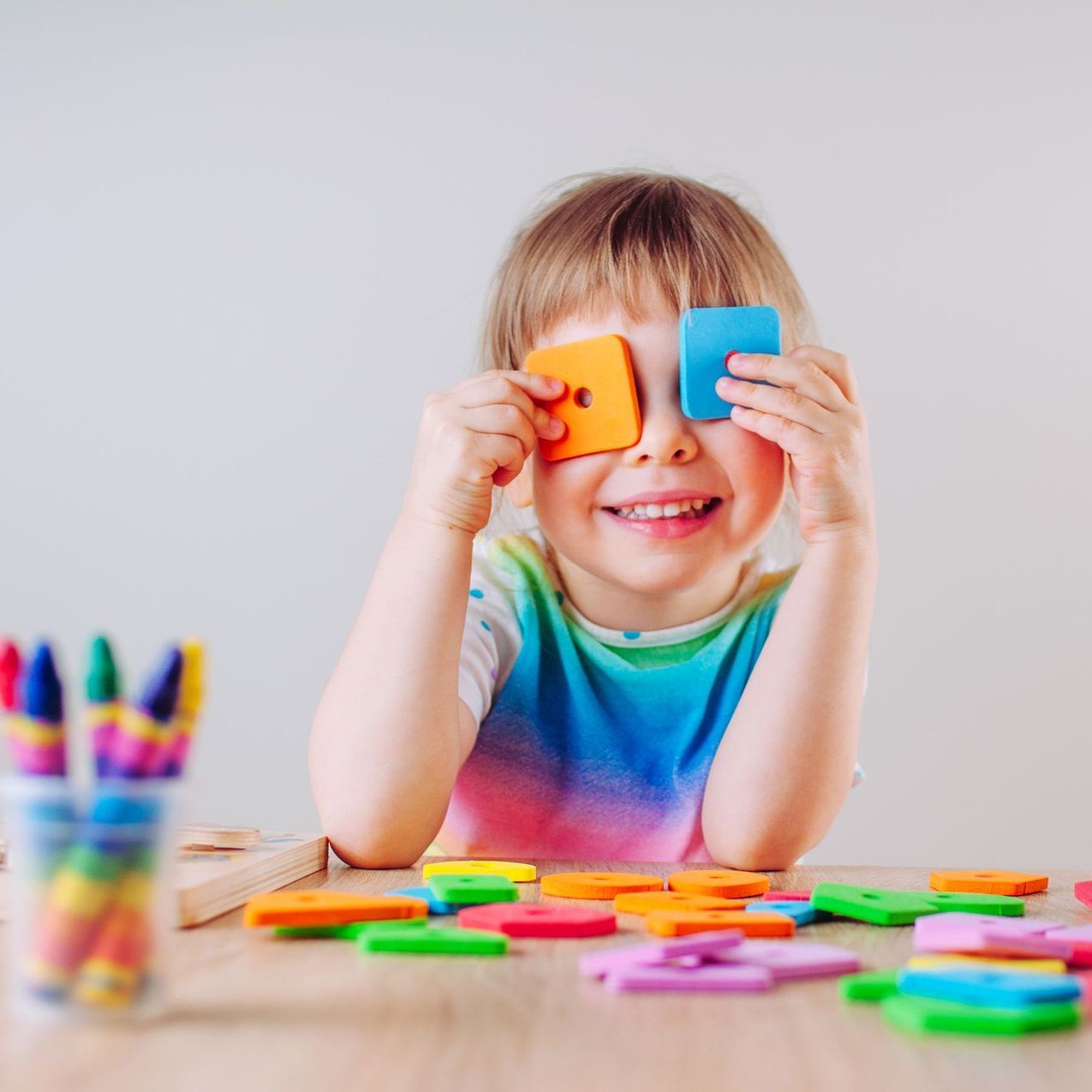 A little girl is sitting at a table playing with scissors and crayons