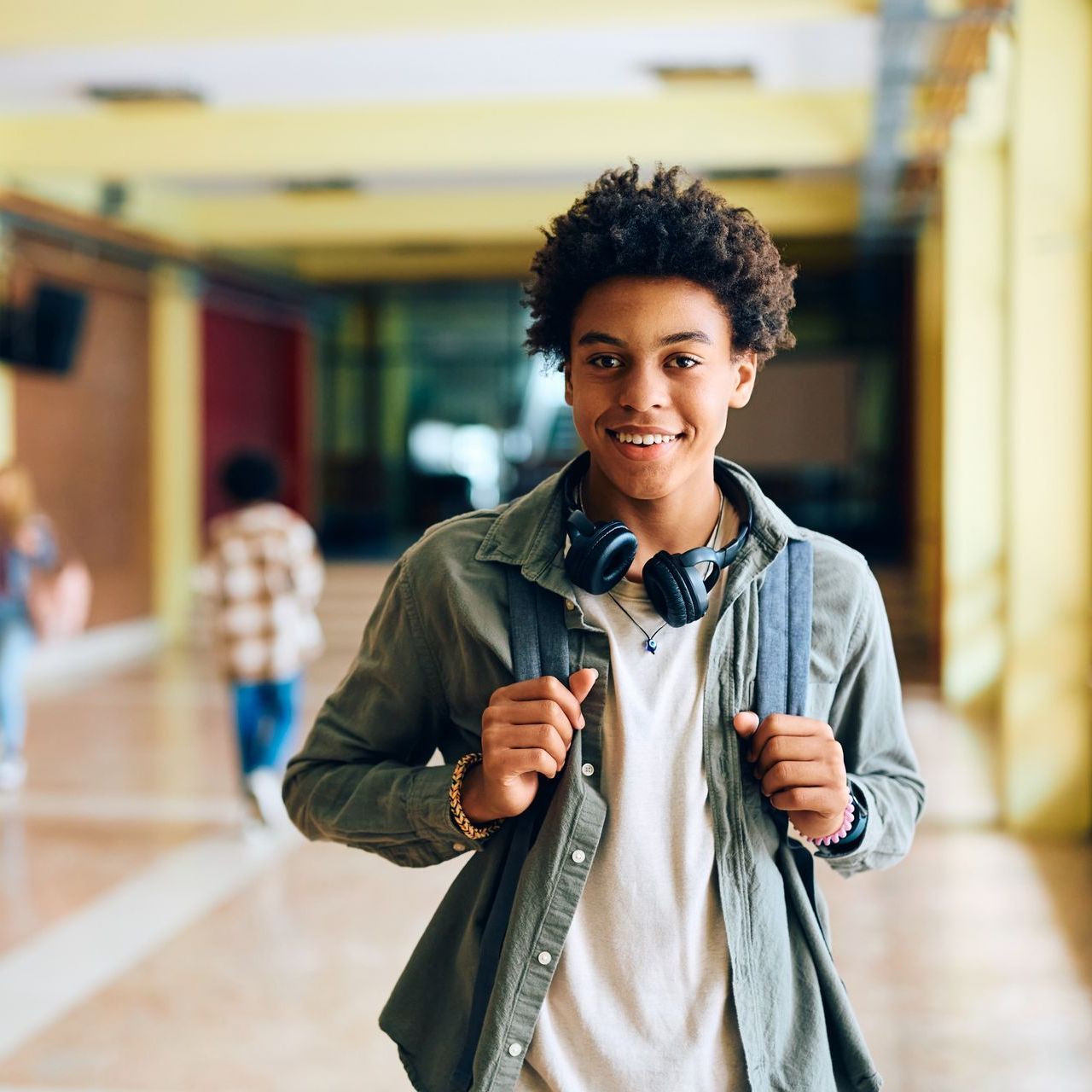 A young man wearing headphones and a backpack is walking down a hallway.