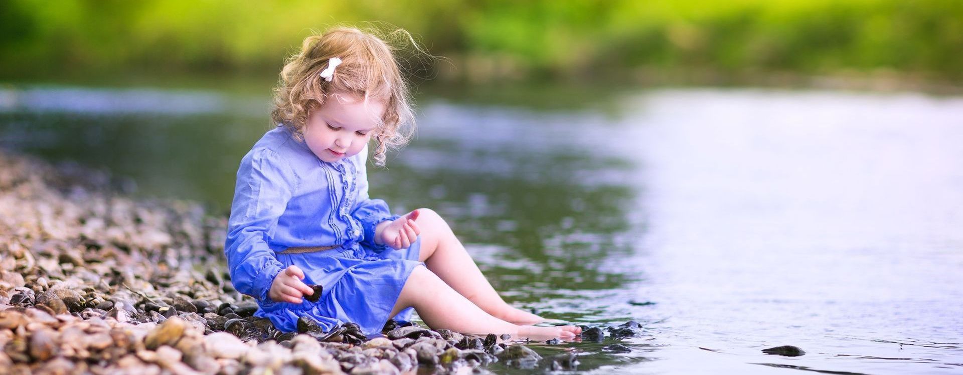 A little girl is sitting on the shore of a river.