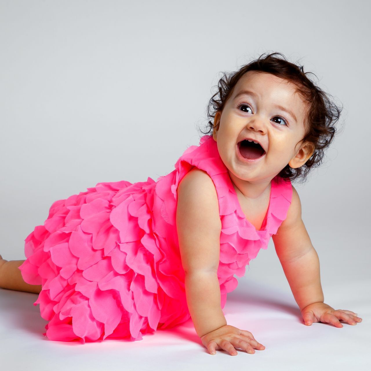 A baby in a pink dress is crawling on the floor