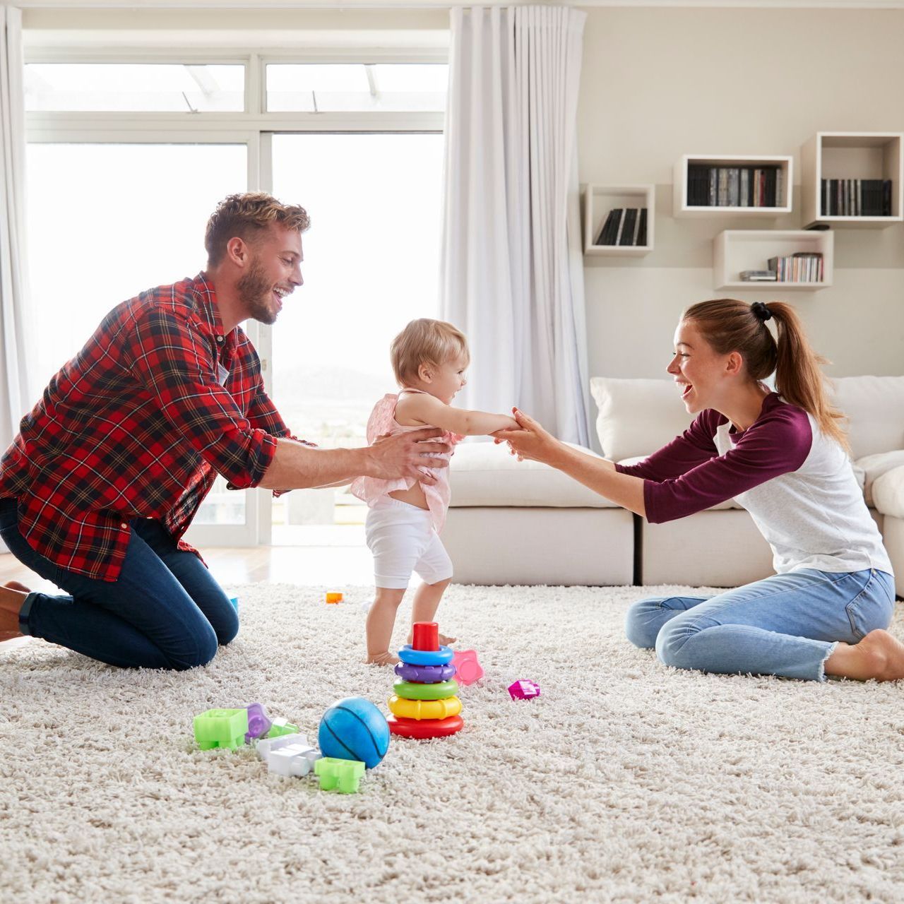 A man and woman are kneeling on the floor playing with a baby.