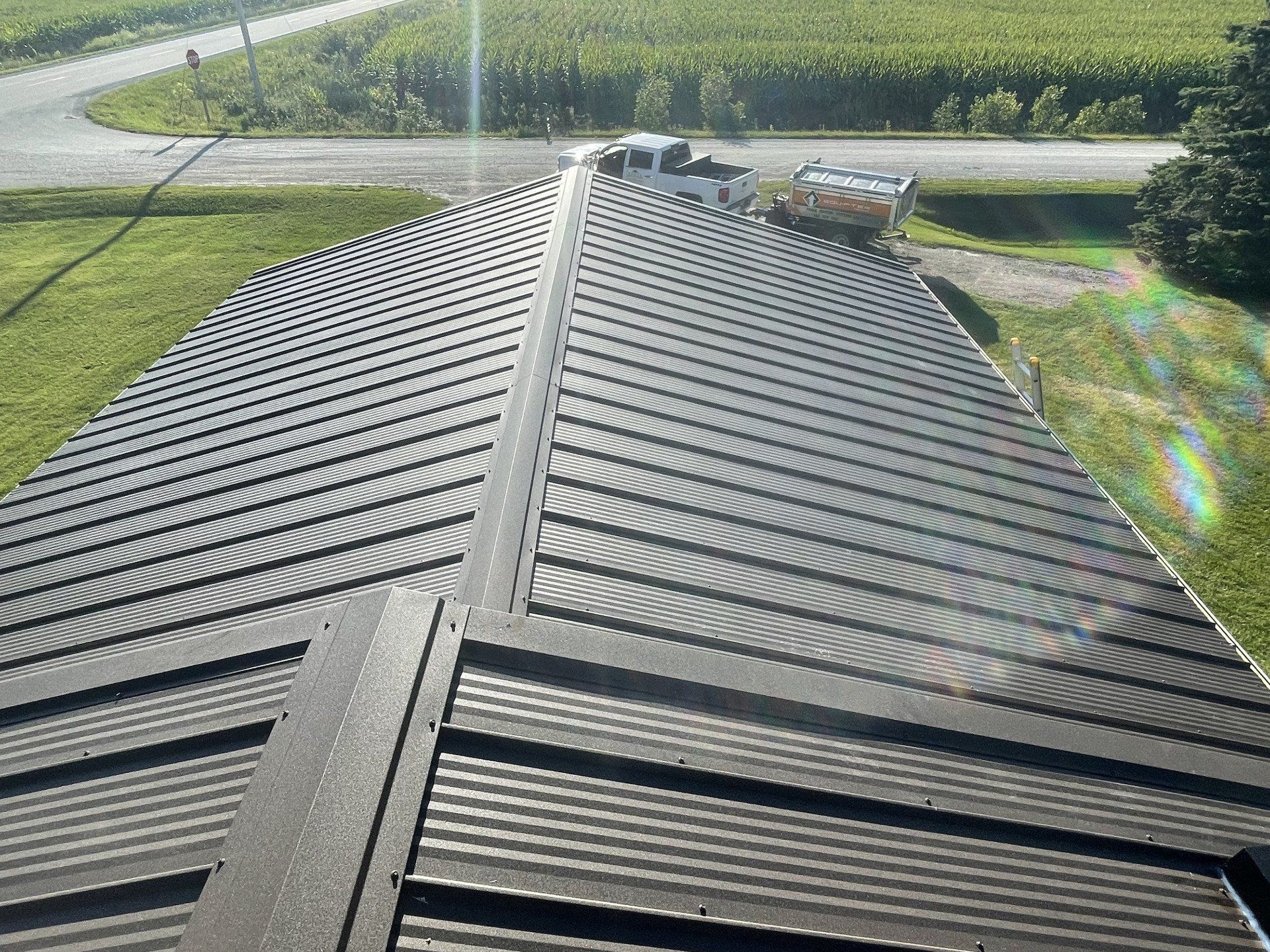 Dark metal roof with a central seam, angled panels, and a rural setting.