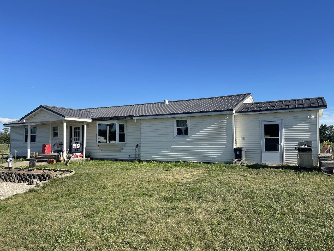 White house with dark roof and porch, set against a blue sky and grassy yard.