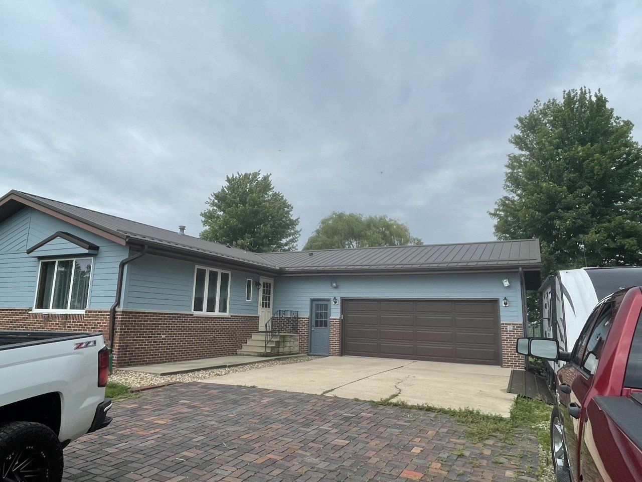 Blue house with brown garage door; red and white trucks parked in driveway. Cloudy sky.