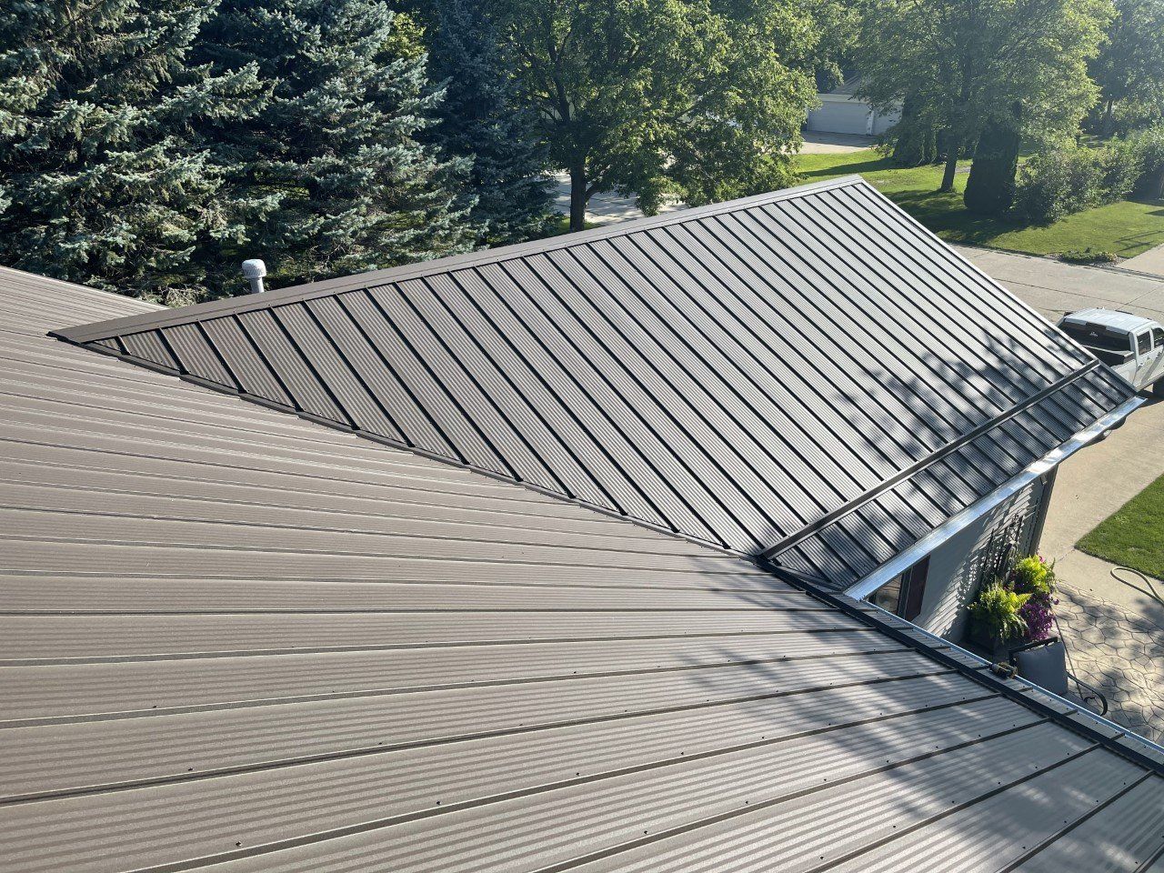 A dark brown metal roof on a residential building, viewed from above on a sunny day.