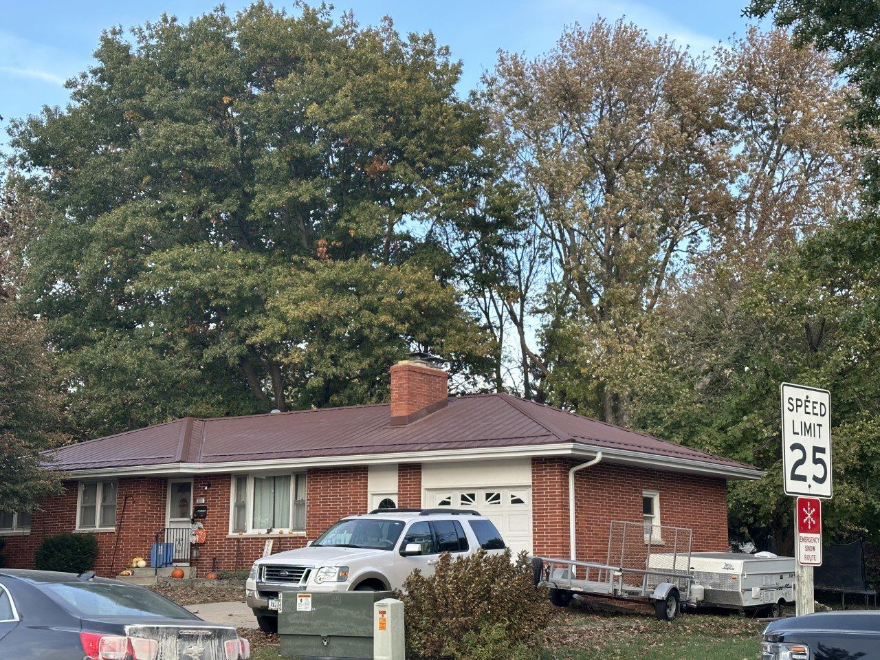 Red brick house with a white SUV in front, a speed limit sign, and trees.