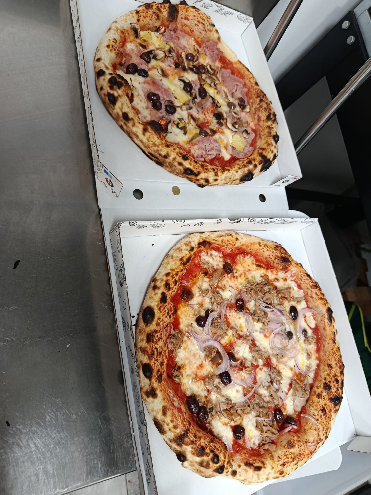 Due scatole per pizza aperte con grandi pizze condite con olive e formaggio su un tavolo scuro