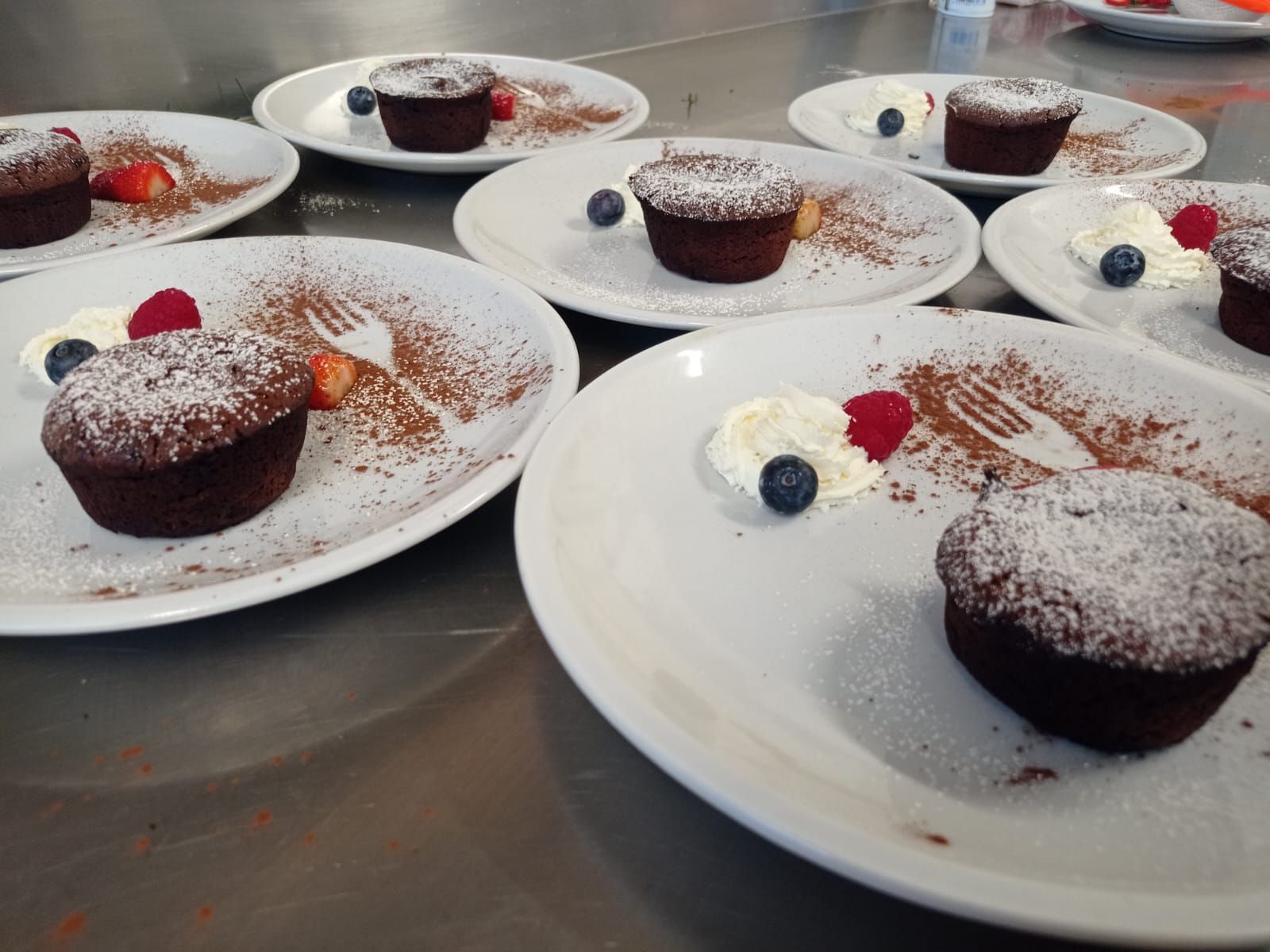 Cupcake al cioccolato su piatti bianchi, spolverati di zucchero a velo e guarniti con frutti di bosco.